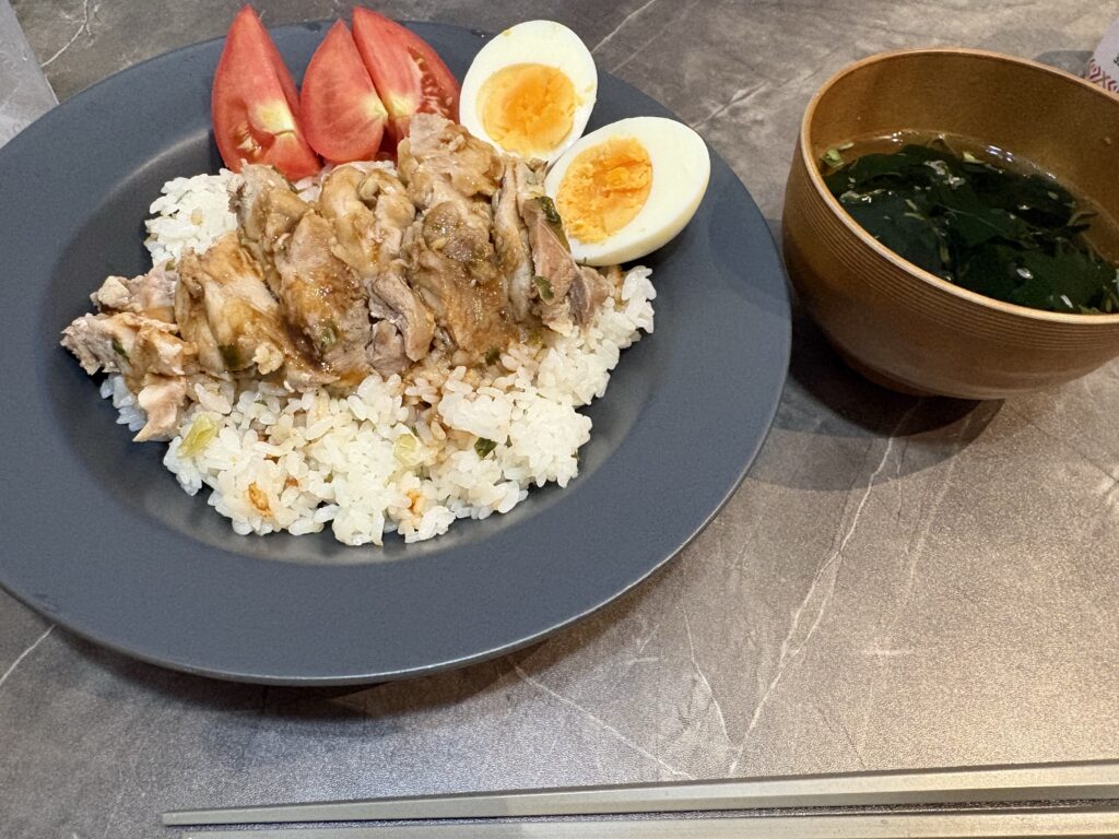 青灰色の皿に盛った鶏むね肉とご飯、トマト、半分に切ったゆで卵。