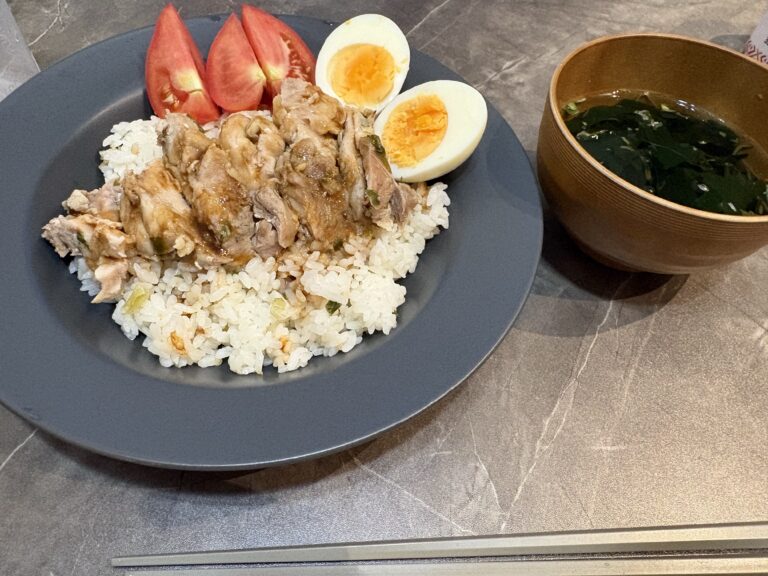 青灰色の皿に盛った鶏むね肉とご飯、トマト、半分に切ったゆで卵。